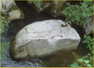 流れる水の働き　～斐伊川たんけんに行こう～　上流　遠いのでわかりづらいのですが　この岩も１０ｍ以上はあります　手前側の面はスパッとまっすぐに切られたようになっています
